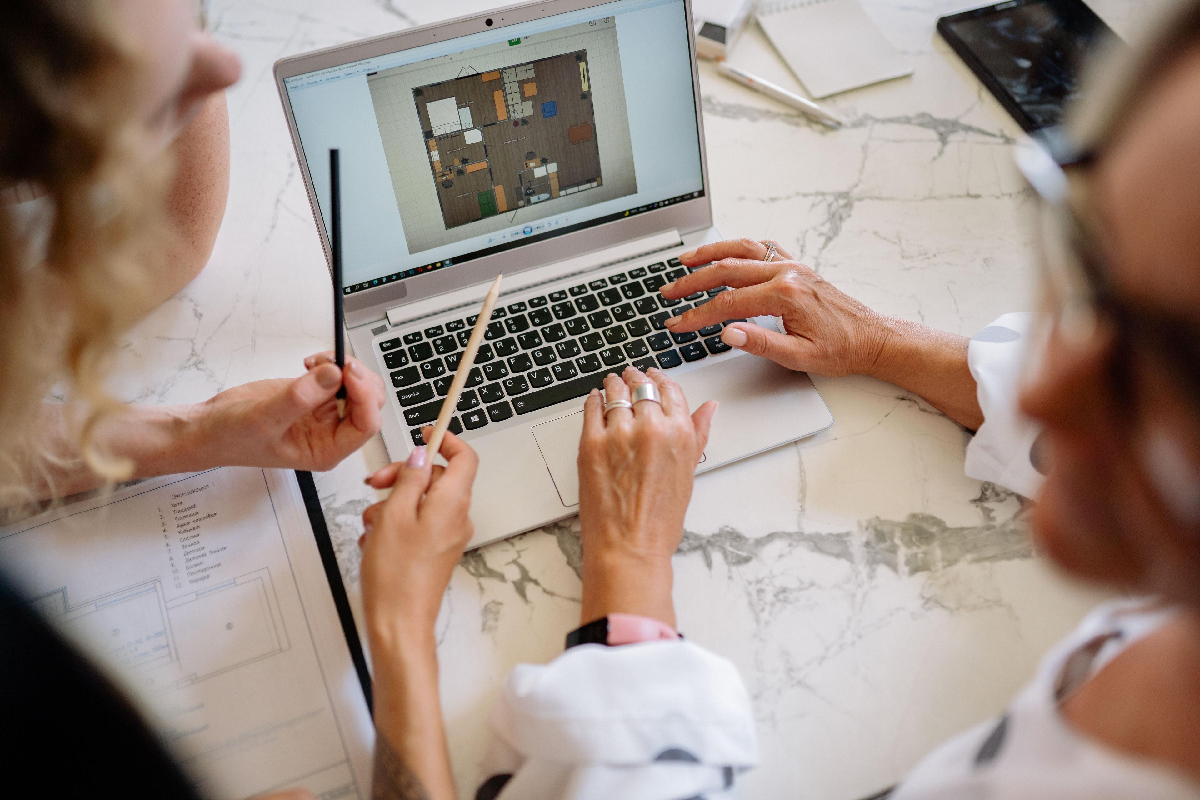 Zwei Personen betrachten gemeinsam einen Laptop mit einer digitalen Grundrissdarstellung auf dem Bildschirm.